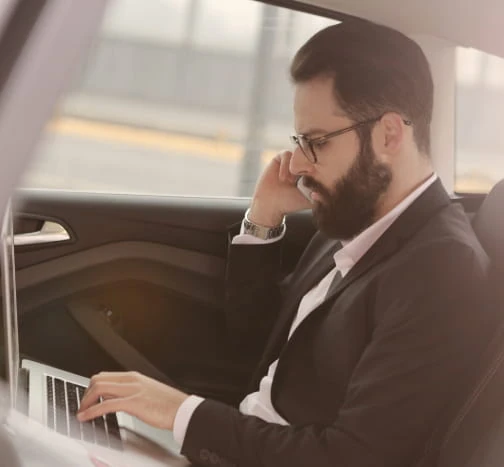 Passager en tenue professionnelle utilisant son téléphone dans une voiture, près d’un ordinateur portable.