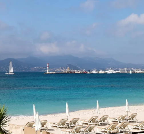 Plage du Var avec des parasols, la mer et des voiliers au large.